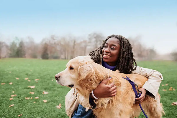 A woman in a field hugging her golden retriever