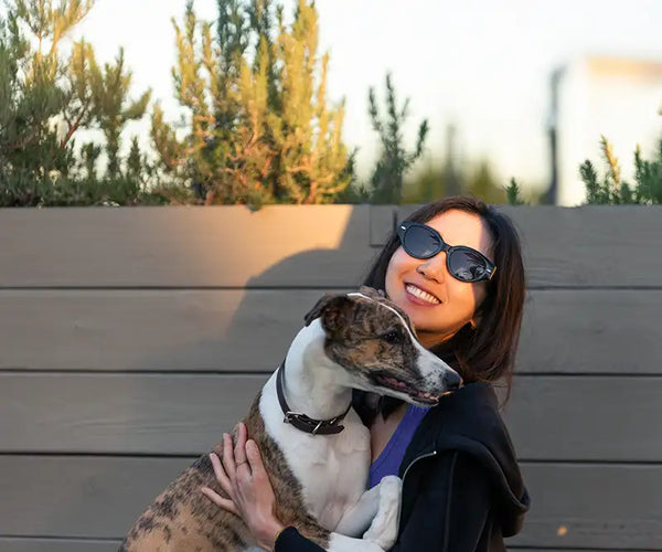 A woman in sunglasses holding a dog against a wood wall